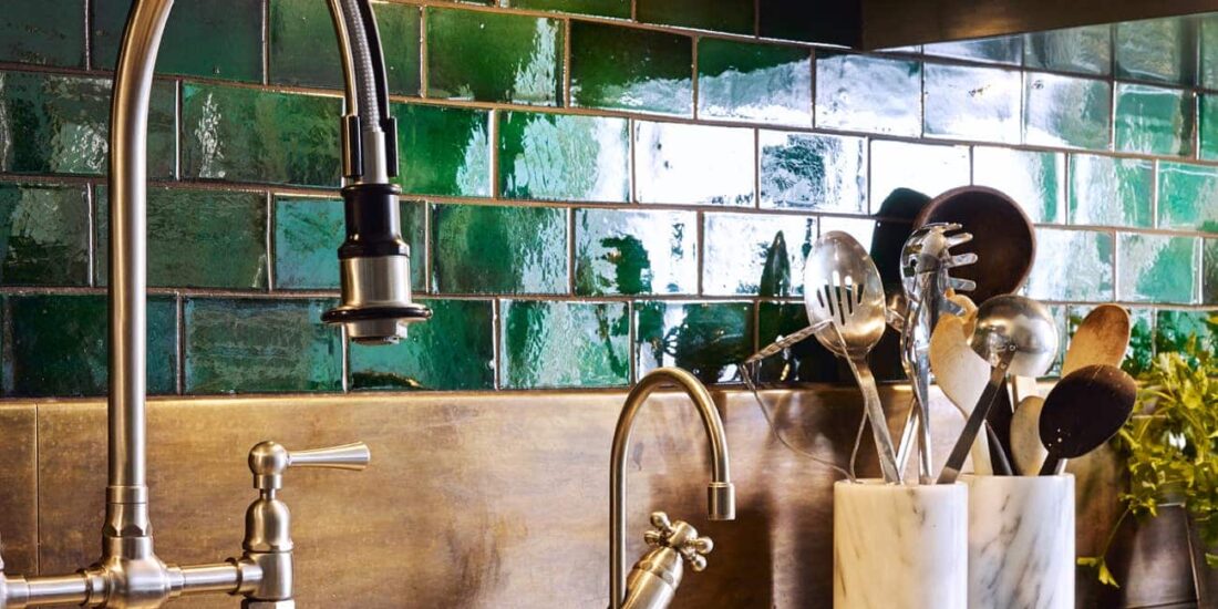 Industrial taps with green wall tiles and wooden splashback