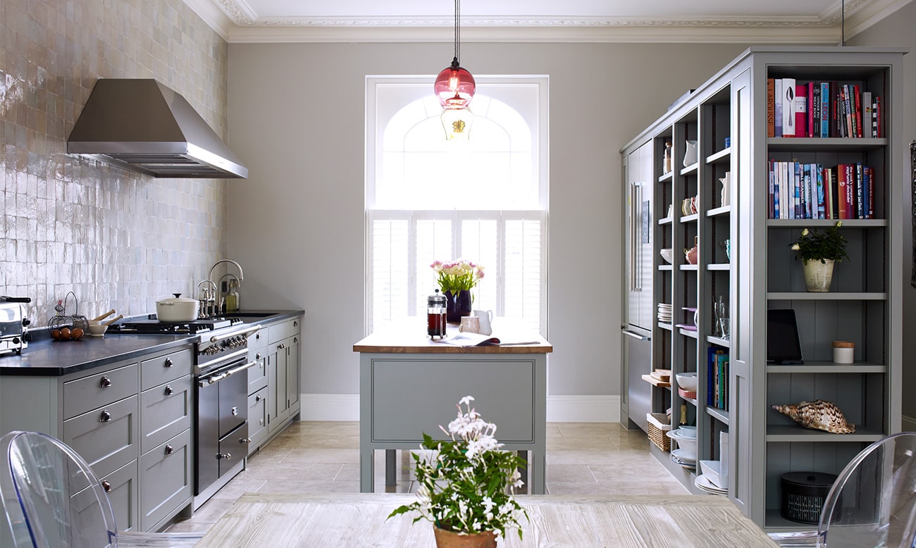 The heritage kitchen range with classic grey cabinets, aga oven, island and bookshelves with built-in fridge.